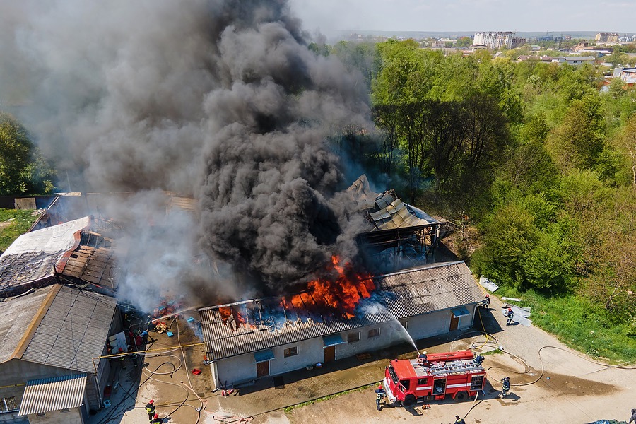 Aerial view of firefighters extinguishing ruined building on fire with collapsed roof and rising dark smoke.